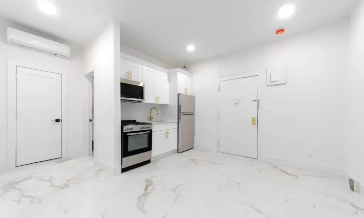 Kitchen/Dining with stainless steel appliances, sink, white cabinets, and a wall unit AC