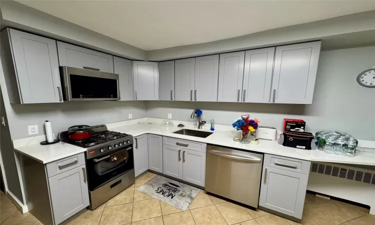 Kitchen featuring appliances with stainless steel finishes, sink, radiator heating unit, and gray cabinetry