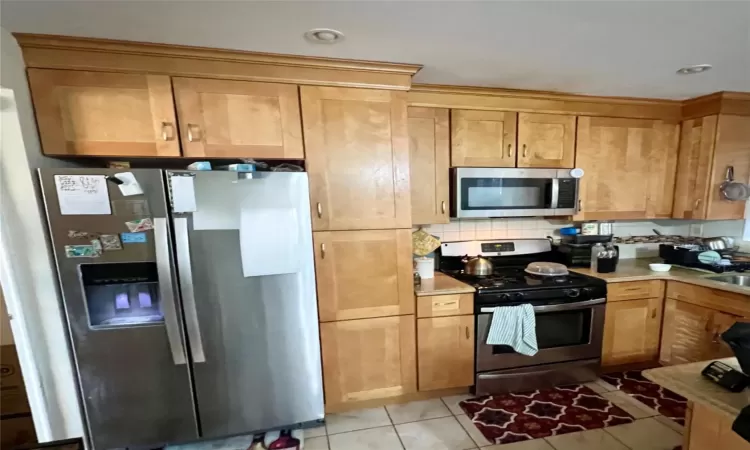 Kitchen with decorative backsplash, appliances with stainless steel finishes, light tile patterned floors, and sink