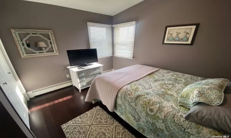 Bedroom featuring hardwood / wood-style flooring, a baseboard radiator, and a closet