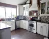 Kitchen featuring white cabinetry, appliances with stainless steel finishes, custom exhaust hood, and backsplash