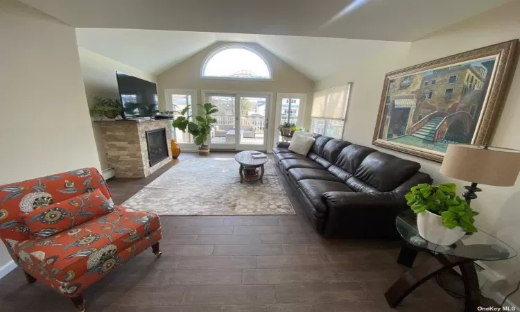 Living room with a stone fireplace, dark wood-type flooring, and lofted ceiling