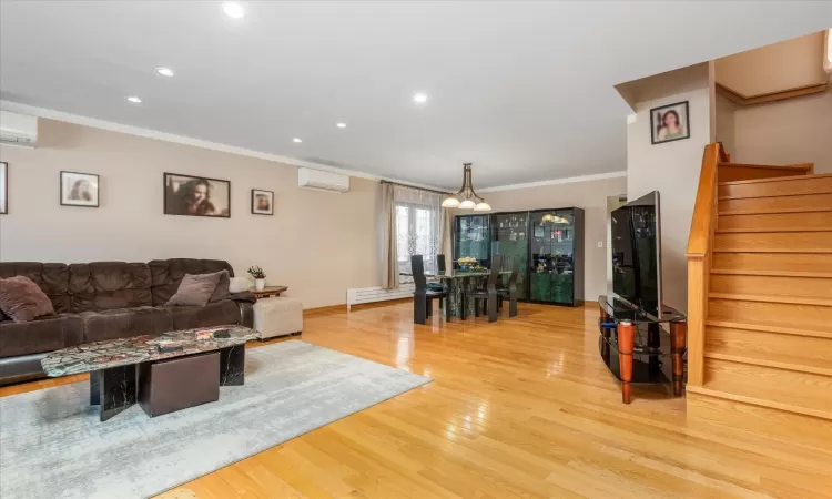 Living room featuring a baseboard radiator, a wall mounted air conditioner, crown molding, a chandelier, and hardwood / wood-style flooring