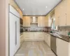 Kitchen featuring sink, built in appliances, wall chimney exhaust hood, dark stone countertops, and light parquet flooring