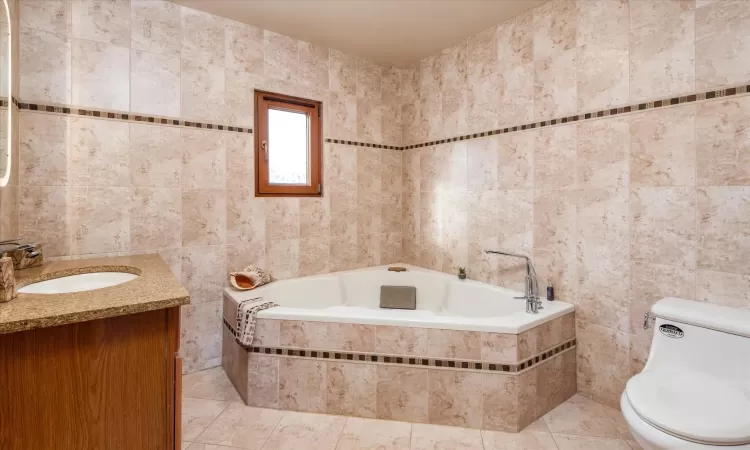 Bathroom featuring tile patterned floors, vanity, tile walls, and toilet