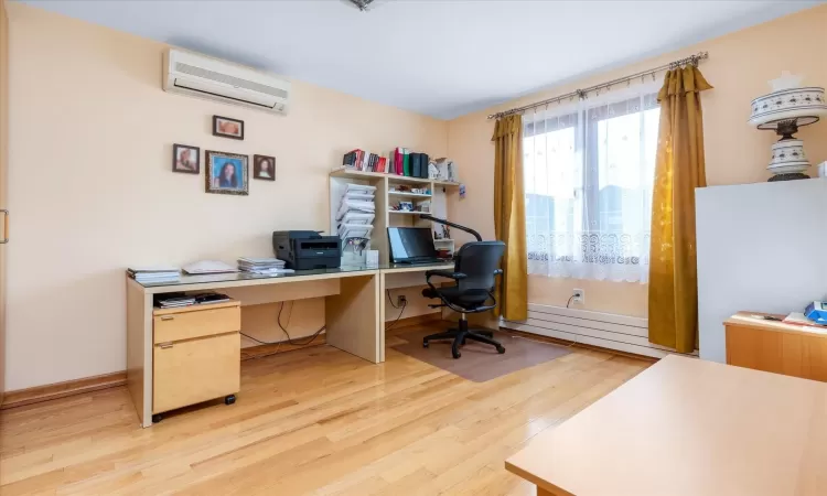 Office area with light hardwood / wood-style floors, an AC wall unit, and a baseboard radiator