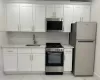 Kitchen with sink, decorative backsplash, white cabinets, and appliances with stainless steel finishes