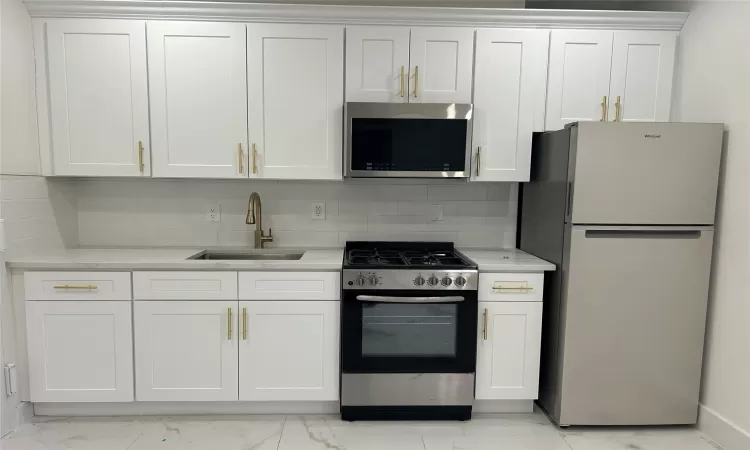 Kitchen with sink, decorative backsplash, white cabinets, and appliances with stainless steel finishes