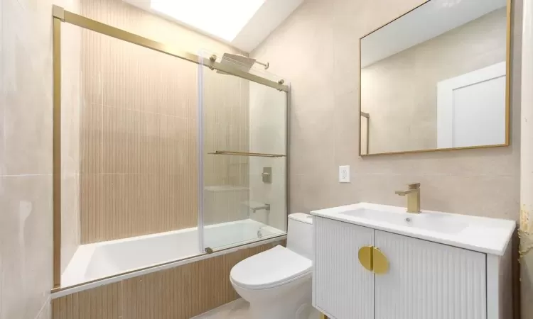 Full bathroom featuring tile walls, vanity, enclosed tub / shower combo, and toilet