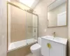 Full bathroom with tile walls, vanity, enclosed tub / shower combo, and toilet