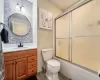 Full bathroom with toilet, tile patterned floors, vanity, and bath / shower combo with glass door