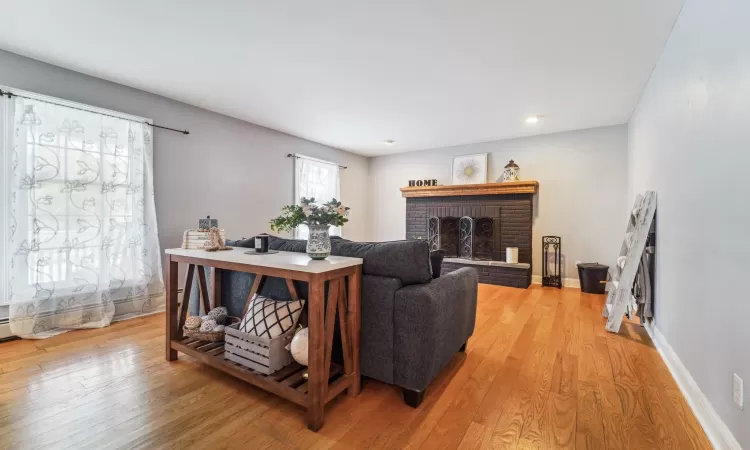 Living room featuring baseboard heating, a brick fireplace, and light wood-type flooring