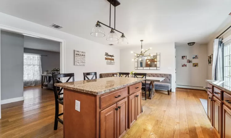 Kitchen featuring pendant lighting, a breakfast bar area, light stone countertops, a kitchen island, and light wood-type flooring