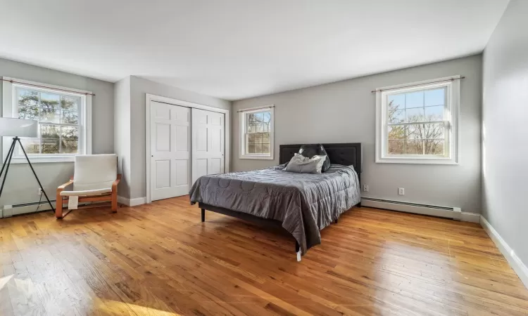 Bedroom with multiple windows, a baseboard heating unit, and light hardwood / wood-style floors