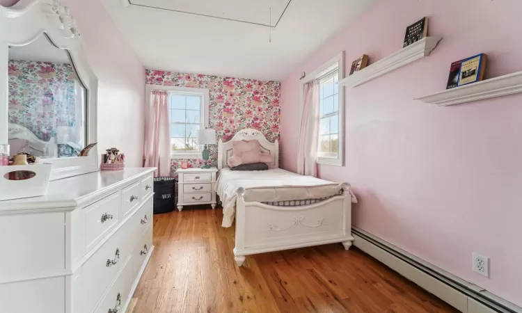 Bedroom featuring multiple windows, a baseboard heating unit, and hardwood / wood-style flooring