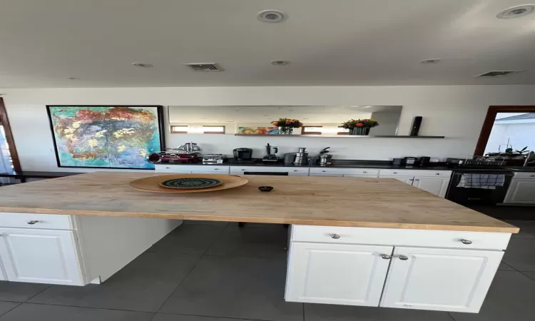 Kitchen with white cabinetry, butcher block countertops, dark tile patterned flooring, and a kitchen island