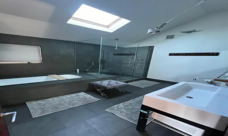 Bathroom featuring vanity, vaulted ceiling with skylight, and independent shower and bath