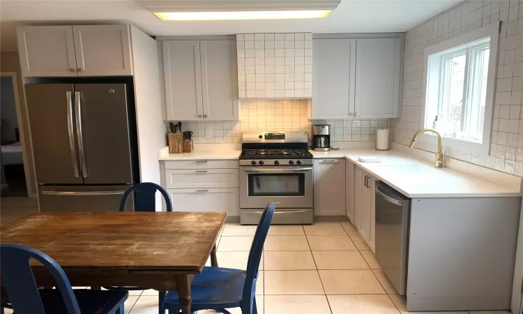 Kitchen featuring light tile patterned flooring, stainless steel appliances, decorative backsplash, and gray cabinetry