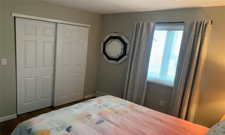 Bedroom with dark wood-type flooring, a closet, multiple windows, and a baseboard heating unit