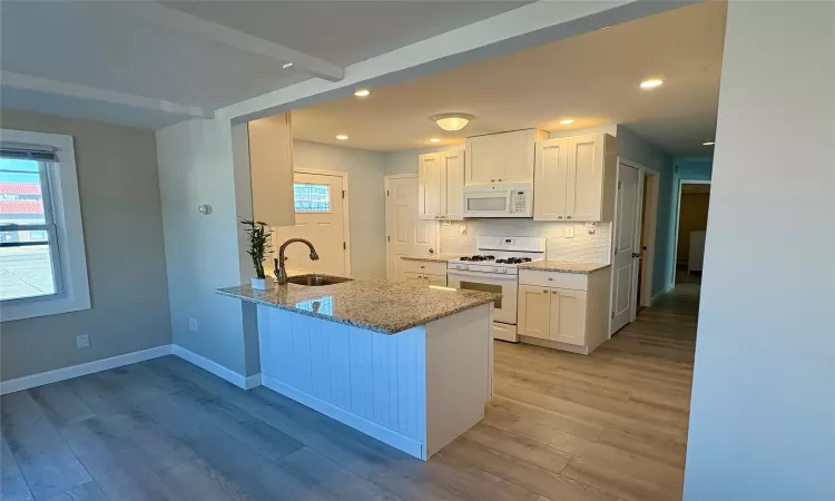 Kitchen with white cabinetry, sink, white appliances, and light stone countertops