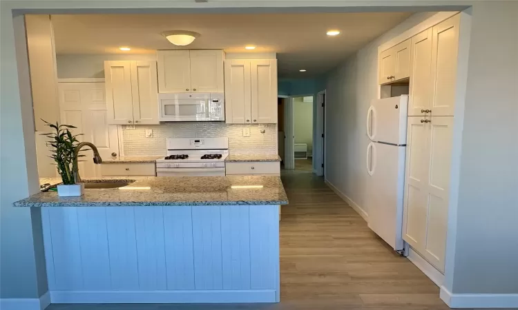 Kitchen featuring sink, white appliances, white cabinets, stone countertops, and kitchen peninsula