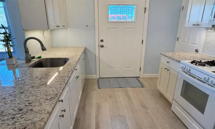 Kitchen with light stone counters, sink, white cabinetry, and white gas range oven