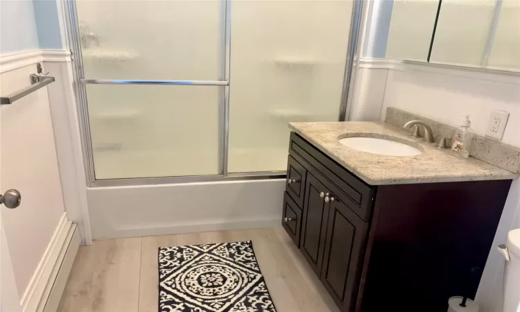 Full bathroom featuring vanity, hardwood / wood-style floors, bath / shower combo with glass door, and toilet