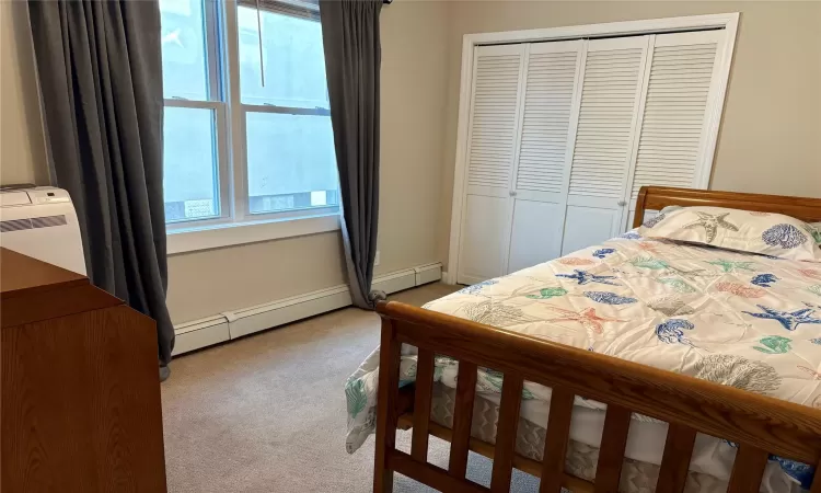 Carpeted bedroom featuring a baseboard heating unit and a closet