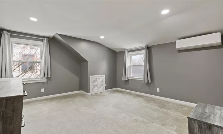 Bonus room featuring light colored carpet, plenty of natural light, a wall unit AC, and lofted ceiling