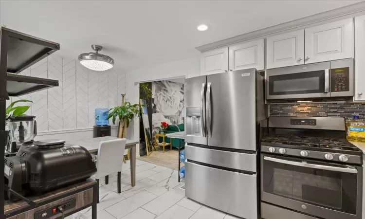 Kitchen with white cabinetry, backsplash, and appliances with stainless steel finishes