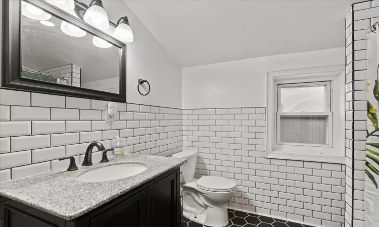 Bathroom with tile patterned floors, vanity, toilet, and tile walls