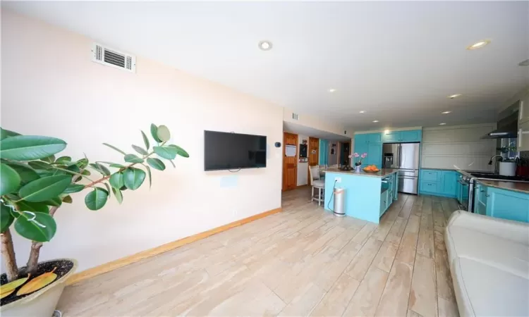 Kitchen with blue cabinets, wall chimney exhaust hood, light hardwood / wood-style floors, and stainless steel appliances