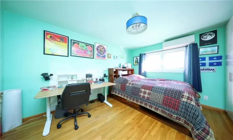 Bedroom with light hardwood / wood-style flooring and an AC wall unit