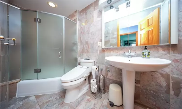 Bathroom featuring bath / shower combo with glass door, tile walls, and toilet