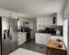 Kitchen with stainless steel appliances, dark vinyl floors, white cabinets, and backsplash