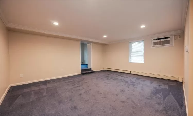 Empty room featuring a baseboard radiator, ornamental molding, a wall unit AC, and dark carpet