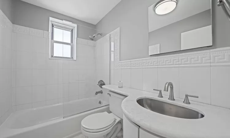 Full bathroom with tile walls, tiled shower / bath, vanity, and toilet