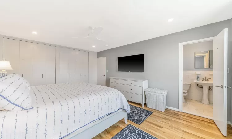 Bedroom with sink, light hardwood / wood-style flooring, ceiling fan, connected bathroom, and two closets