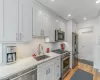 Kitchen with sink, white cabinetry, premium appliances, light stone countertops, and light hardwood / wood-style floors