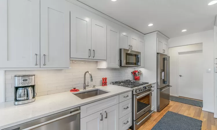 Kitchen with sink, white cabinetry, premium appliances, light stone countertops, and light hardwood / wood-style floors