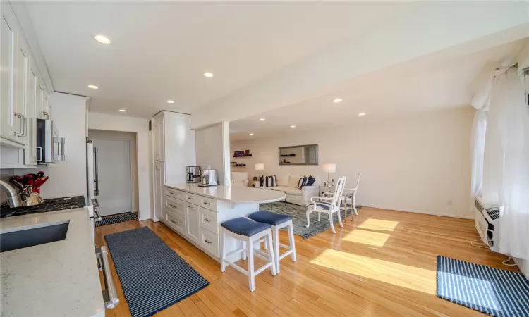 Kitchen with a kitchen bar, white cabinetry, kitchen peninsula, light stone countertops, and light hardwood / wood-style floors