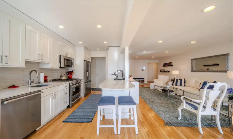 Kitchen featuring sink, white cabinetry, premium appliances, a kitchen breakfast bar, and backsplash