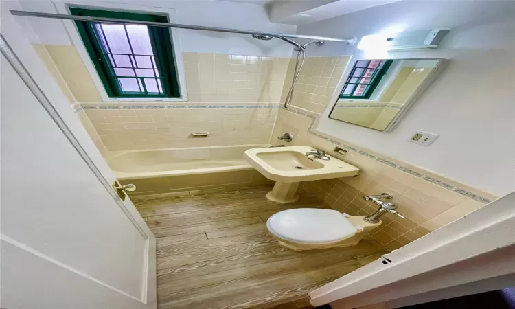 Full bathroom with hardwood / wood-style floors, tile walls, toilet, and tiled shower / bath