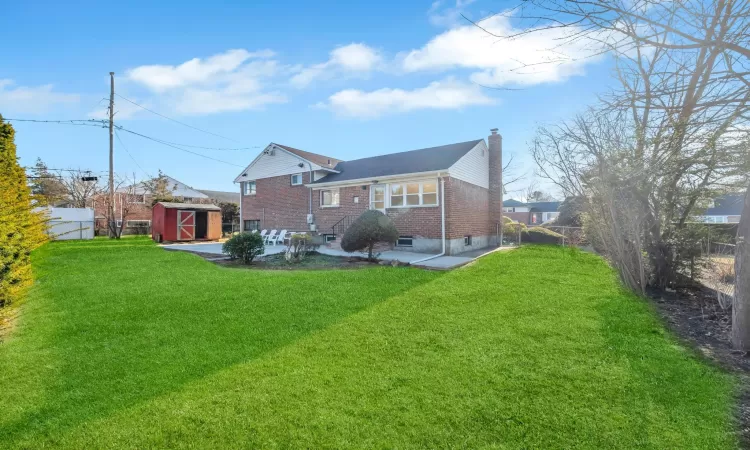 Rear view of house featuring a patio area, a lawn, and a storage shed