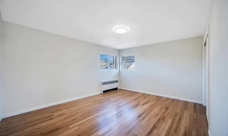 Unfurnished bedroom with radiator heating unit and light hardwood / wood-style flooring