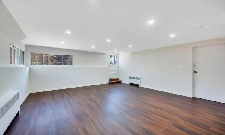 Empty room with dark wood-type flooring and radiator heating unit