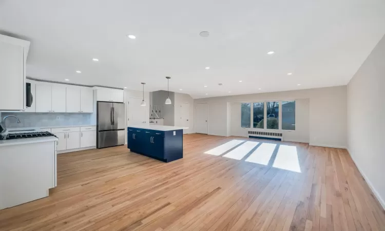 Kitchen with pendant lighting, blue cabinetry, a kitchen island, radiator heating unit, and stainless steel refrigerator