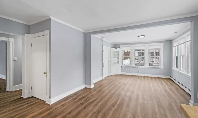 Empty room featuring dark wood-type flooring, crown molding, and baseboard heating