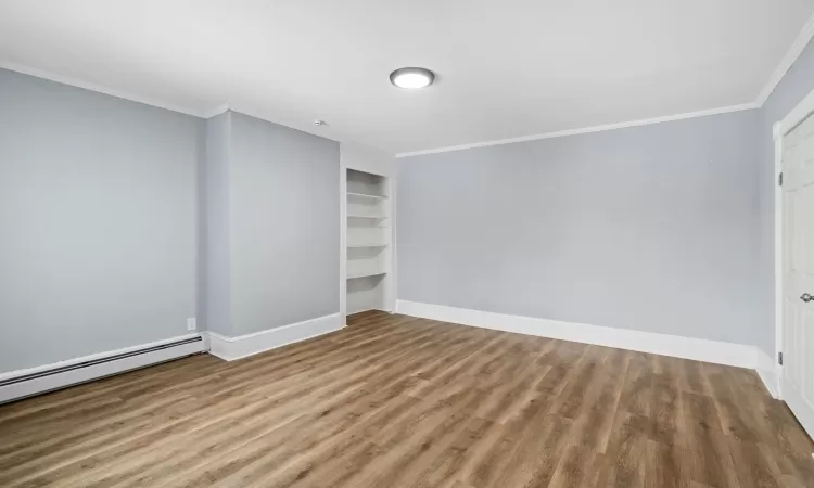 Spare room featuring ornamental molding, wood-type flooring, a baseboard heating unit, and built in features