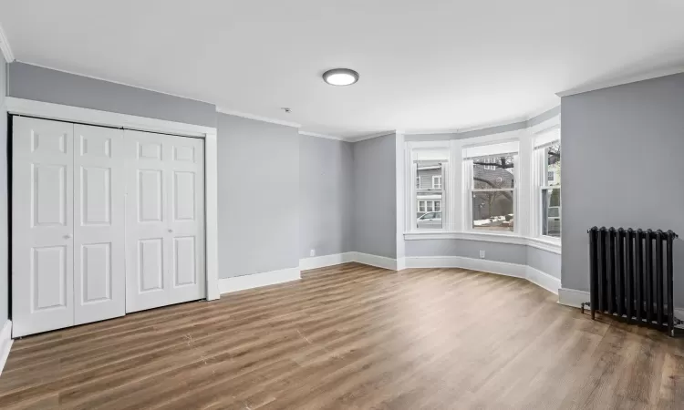 Unfurnished bedroom featuring dark hardwood / wood-style floors, crown molding, radiator heating unit, and a closet